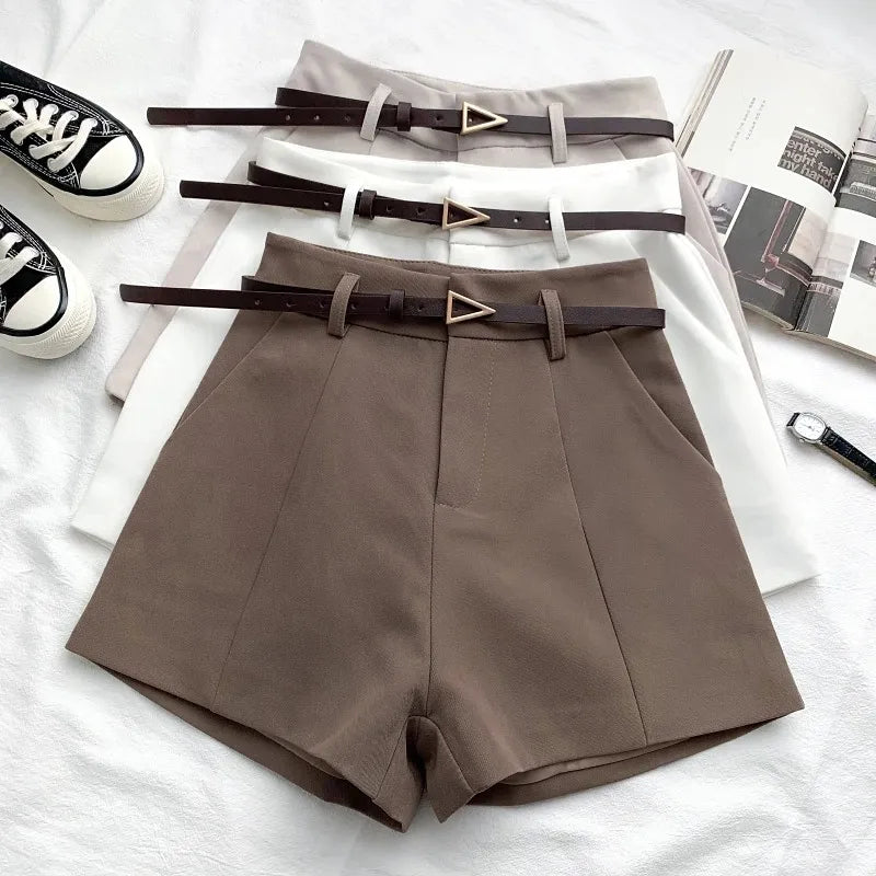 Brown shorts with belts on a white surface with shoes and magazines.