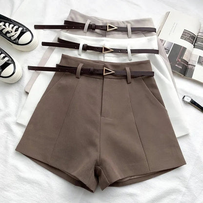 Brown shorts with belts on a white surface with shoes and magazines.